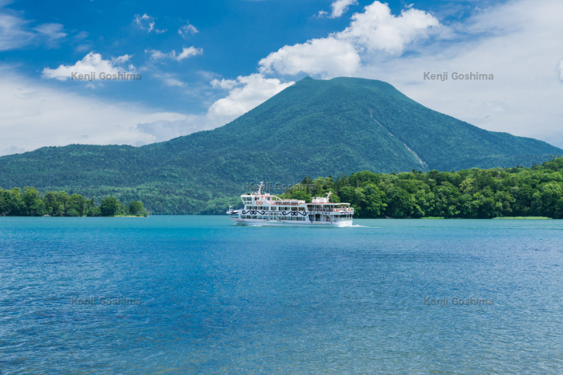 A steaming bowl of ramen noodles, including slices of pork, corn, and green onions.